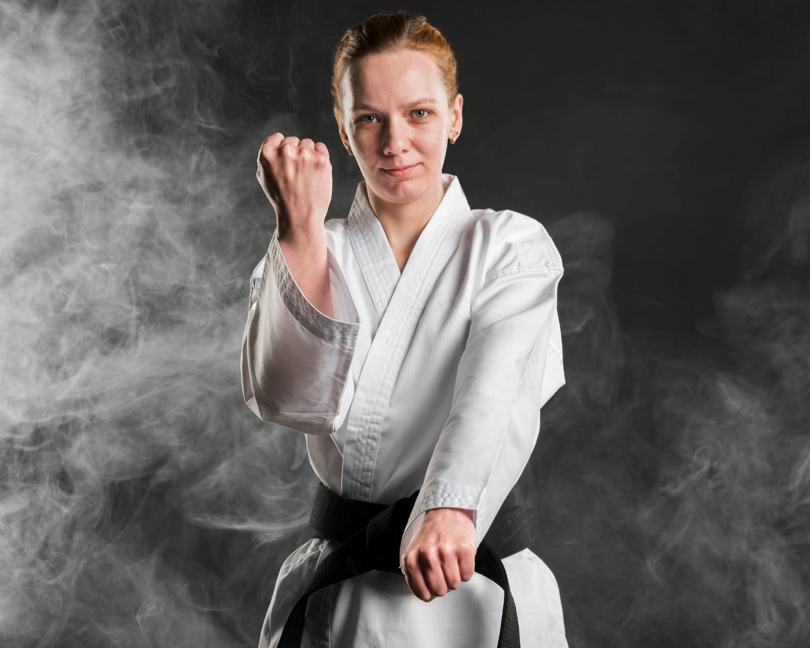A student in a white gi and black belt holding a raised-fist stance during a drill.