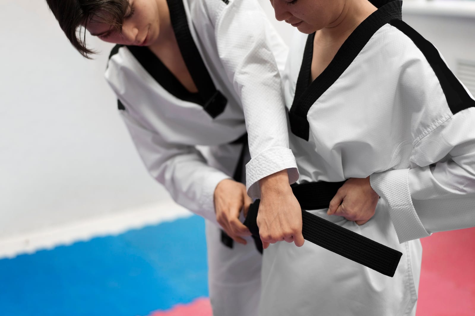 Two students tying their belts over white training uniforms before a session.