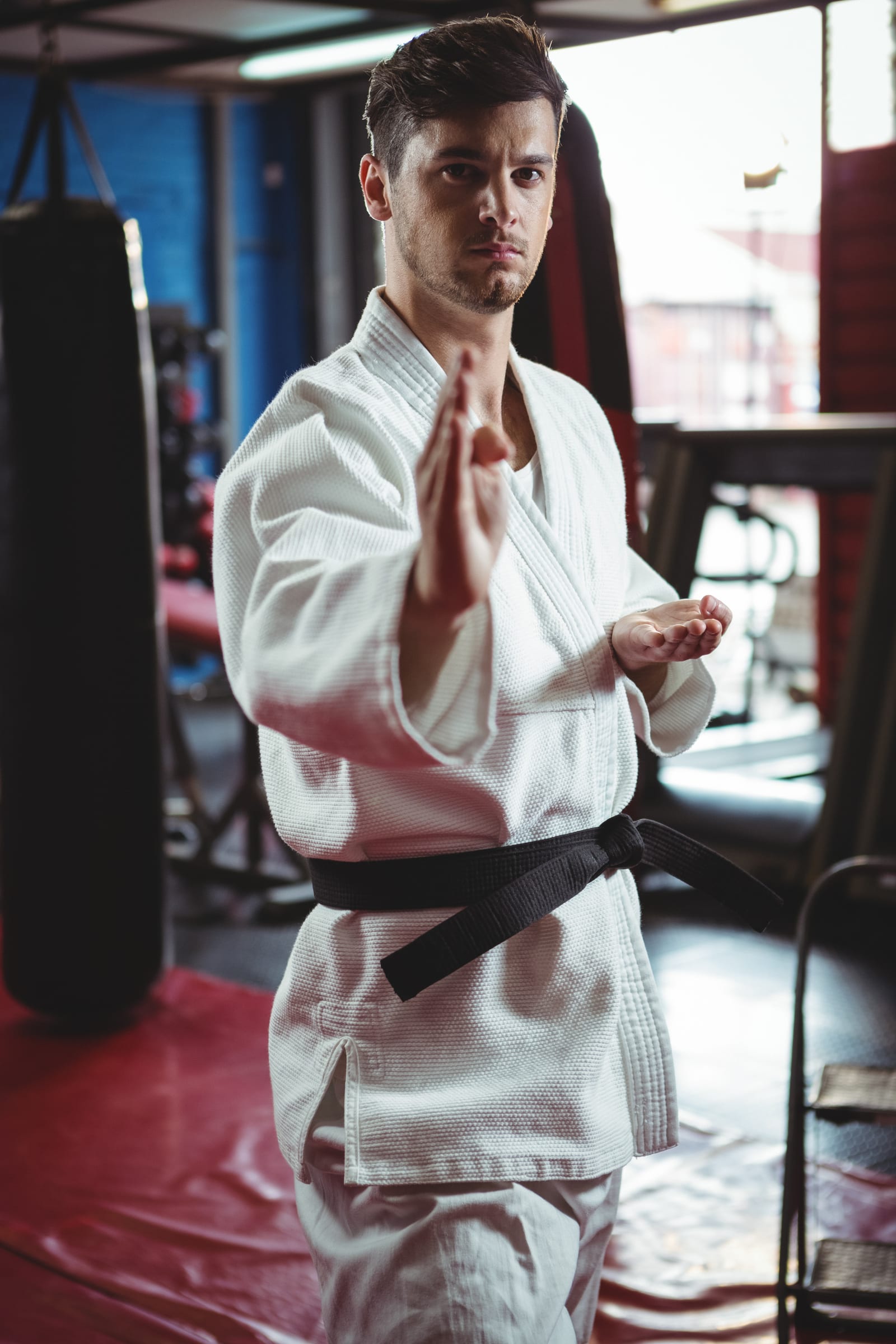A student in a white gi holding an open-hand guard position among heavy bags.