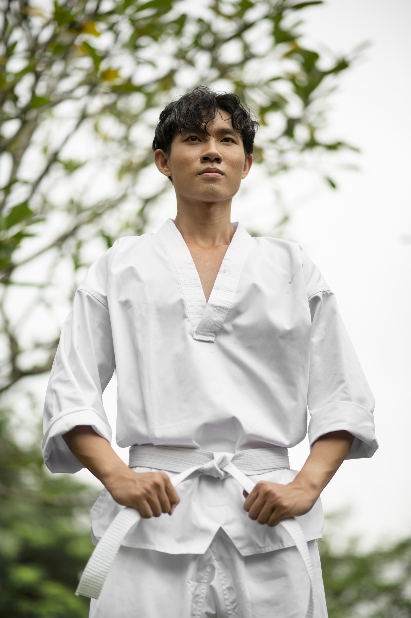 A martial artist standing at attention outdoors among trees before an outreach session.